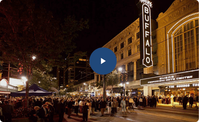 Thumbnail of Shea's Performing Arts Center at night, with a crowd of people gathered outside. The building is lit up, and the "BUFFALO" sign is visible. A play button is superimposed on the image.